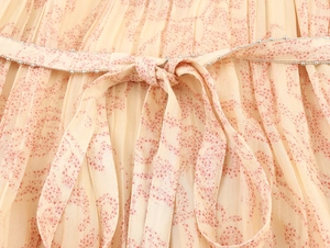 Dettaglio vestito beige a pieghe con stampa floreale rossa e fiocco con perline