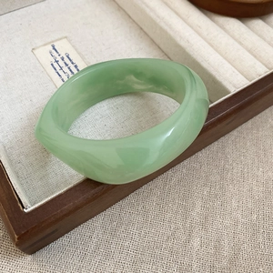 Close-up of thick light green faux jade resin bangle on a wooden jewelry display case