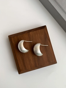 Macro shot of silver crescent stud earrings with brushed metal texture on wooden display