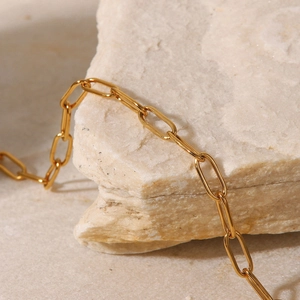 Detail of 18K gold paperclip chain anklet on a natural stone textured background
