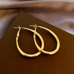 Macro shot of large polished gold teardrop hoop earrings with elegant metal texture