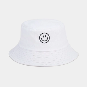 Détail d'un chapeau bob blanc en coton avec un motif de visage souriant brodé noir