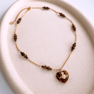 Detailed shot of tiger eye heart pendant with Saturn logo on golden beaded chain
