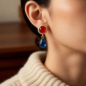 Detail of vintage style drop earrings with red and blue resin stones in a gold finish