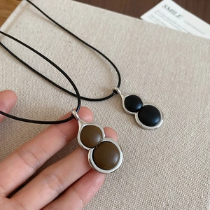 Close-up of leather gourd pendants in silver frames on black cord necklaces