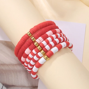 Close-up of bohemian layered clay bead bracelets with red and gold spacers