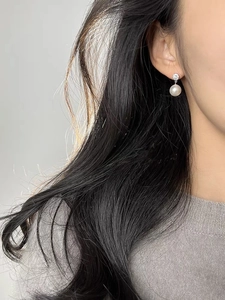 Close-up of elegant round pearl earrings with sparkling zircon studs on female model
