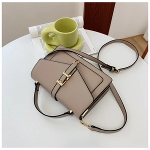 Detail view of khaki leather crossbody bag with gold buckle on a white table