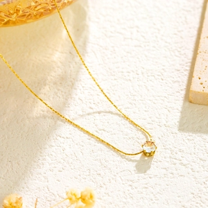 Macro detail of minimalist gold pendant necklace featuring a round zircon in four-prong setting