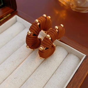 Macro view of C-shape earrings with brown woven texture and gold bead details
