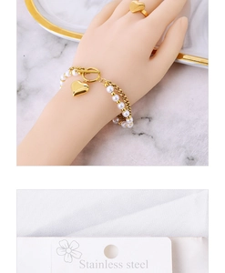 Detailed view of a gold heart ring and pearl chain bracelet with stainless steel OT clasp
