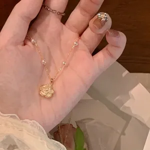 Elegant gold necklace with white rose pendant and small pearl accents held in hand
