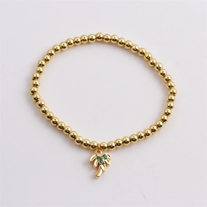 Détail d'un bracelet doré à perles avec un pendentif palmier serti de zircons verts