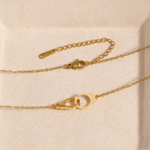 Collana con ciondolo a manette dorate su un vassoio per gioielli beige strutturato