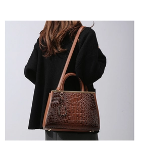 Detail shot of brown crocodile pattern handbag with gold hardware and metal pendant