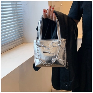 Silver wrinkled tote with bow details and bead chain shown by model near window