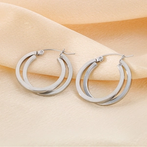 Detailed close-up of silver crisscross titanium steel hoop earrings on beige silk fabric