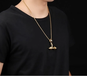 Detail of a golden dumbbell pendant necklace on a black shirt for fitness lifestyle