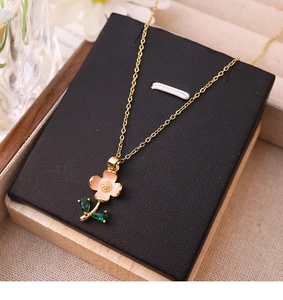 Macro shot of gold necklace with pink flower pendant and green leaf detail on black pad