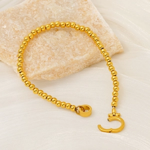 Détail d'un bracelet à perles dorées avec boucle ronde sur un tissu satiné souple