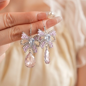 Detail of silver bow earrings with pink teardrop crystals held by a hand