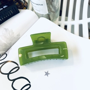 Close-up of emerald green rectangular hair claw clip with transparent finish on paper