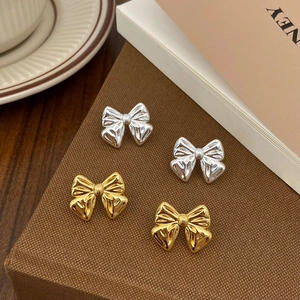 Close-up of gold and silver bow stud earrings with textured metallic finish on a display