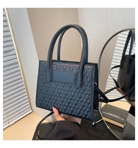 Détail du sac noir montrant la texture géométrique 3D et les doubles poignées rondes