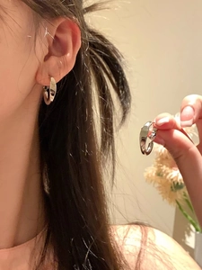 Detailed view of mid-sized silver hoop earrings worn on ear with polished metallic finish
