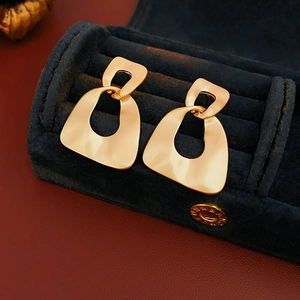 Macro detail of matte gold geometric hollow earrings inside a blue velvet jewelry box
