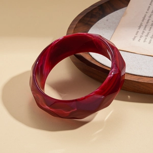 Detail view of deep red faceted resin bangle with marble texture and geometric cut