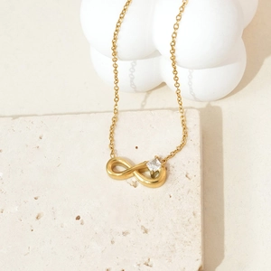 Detail of gold infinity pendant necklace with zircon on a travertine stone surface