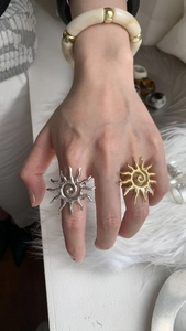 Detailed close-up of a sun-shaped open ring in gold and silver finish on a finger