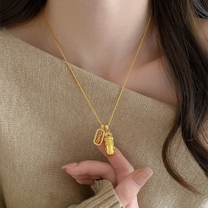 Dettaglio della collana dorata con doppio pendente e zirconi su un maglione beige