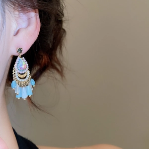 Close-up of bohemian tassel earrings with blue beads and teardrop crystals on model