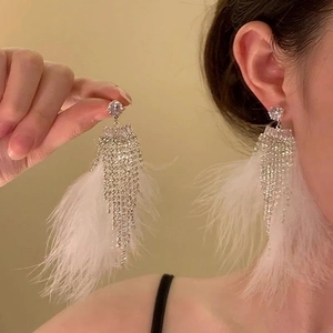 Close-up of long white feather tassel earrings with sparkling rhinestone studs on model