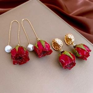 Macro detail of red rose earrings with gold chains and white faux pearl drops
