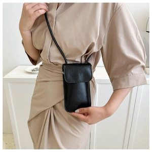 Detail of minimalist black patent leather crossbody mobile bag worn over a beige dress