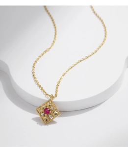 Close-up of a gold rhombus pendant with red gemstone and diamonds on a white base