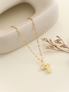 Close-up of golden cross necklace with ruby-colored stone on white ceramic decor