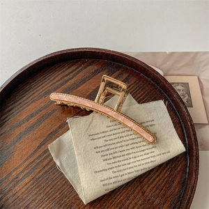 Golden metal hair claw clip with pink marble inlay displayed on a vintage tray