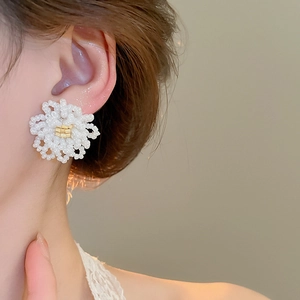 Close-up of elegant handmade beaded floral earrings worn by a model in warm light