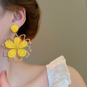 Close-up of a model wearing large yellow woven raffia flower earrings with gold metal trim
