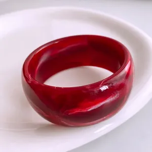 Bague acrylique rouge foncé avec texture marbrée sur une assiette blanche élégante