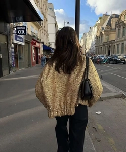 Dettaglio macro della texture con paillettes dorate sul cardigan in maglia da donna