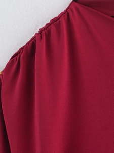 Close-up of deep red knitted fabric with detailed stitching and pleated design texture