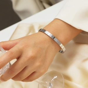 Dettaglio del bracciale in metallo strutturato argento al polso su sfondo di seta fine