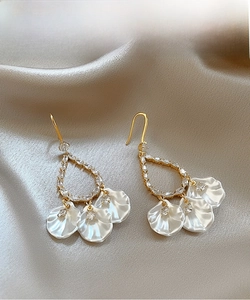 Détail de boucles d'oreilles pendantes dorées avec pendentifs coquillages sur soie