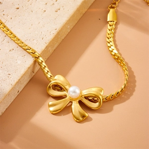 Detailed shot of a gold-plated stainless steel snake chain bracelet with pearl and bow charm