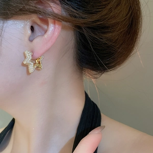 Macro shot of gold star hoop earrings with sparkling cubic zirconia on a model's ear